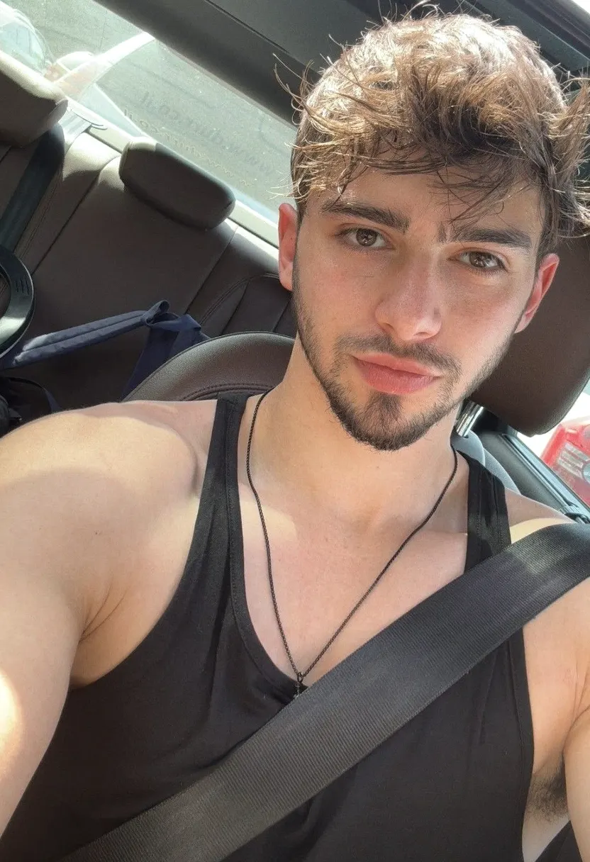 Young man with tousled brown hair taking a close-up selfie in a car.