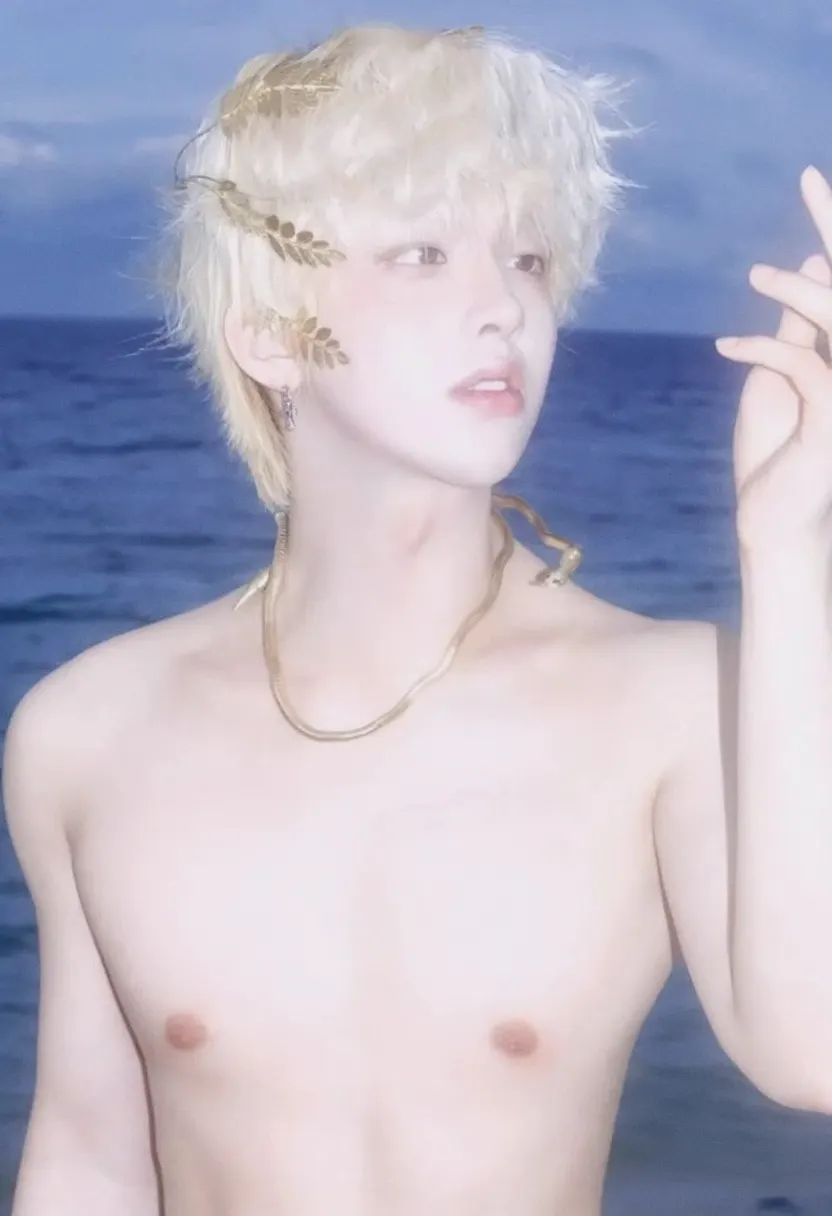 Pale blond person with leaves in their hair by the ocean.